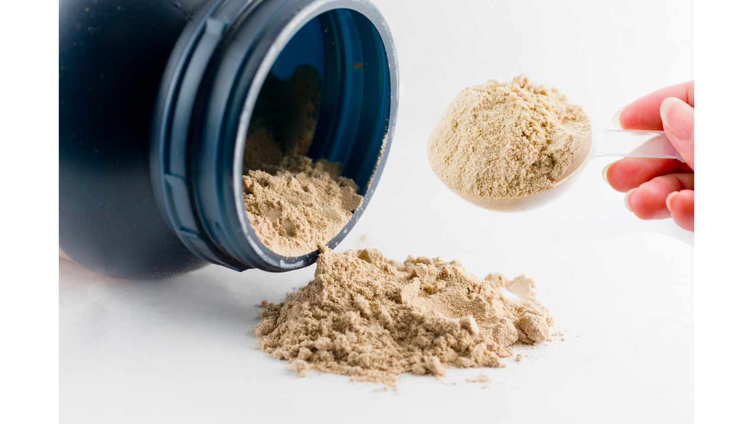 Black plastic bottle with chocolate whey powder poured out in a small pile, with hand holding round scoop of chocolate powder